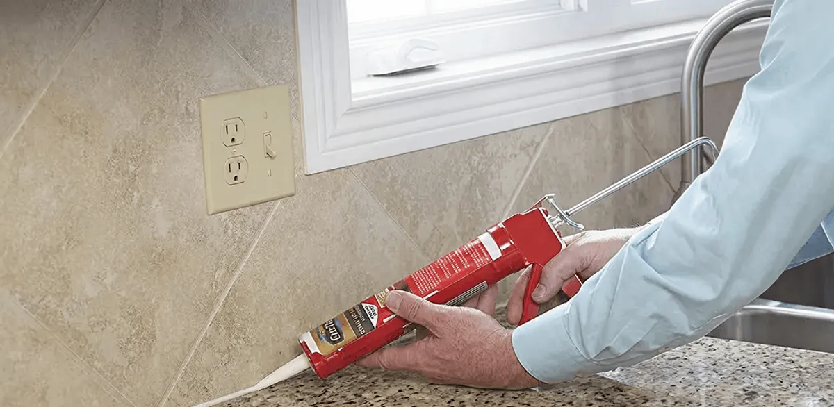 Handyman applying caulk along a kitchen backsplash and countertop seam in Tempe, AZ