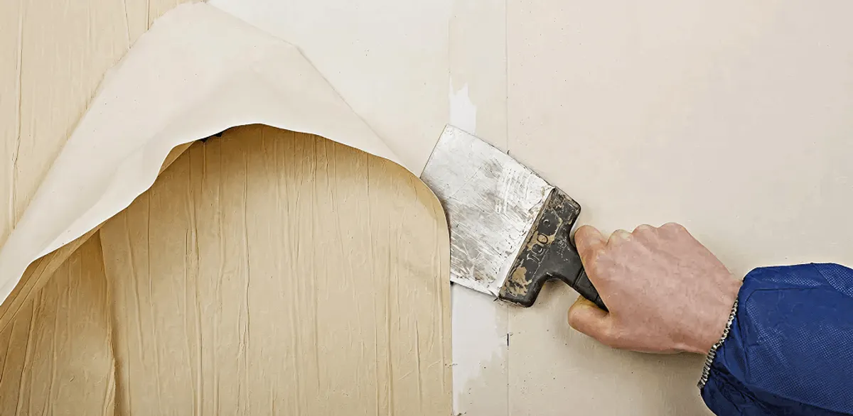 Handyman removing wallpaper with a scraper for wall preparation in Tempe, AZ
